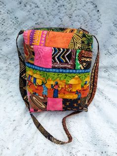 This lovingly handcrafted handbag evokes the feel of an African Village as women and children dance their way through a field of sunflowers and around the circumference of the bag. The artist has paired bold geometrics, animal prints, and symbols to create the perfect backdrop for the centerpiece story print design. This is more than a messenger or crossbody bag. It’s an homage to all of our ancient roots.  1 of 1