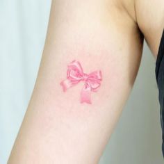 a woman's arm with a pink bow tattoo on the left side of her arm