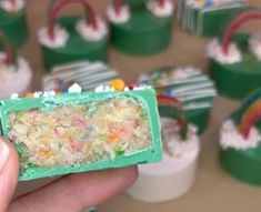 a person holding up a piece of cake in front of cupcakes with rainbow decorations on them