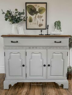 a white dresser with wooden top and drawers in a living room next to a potted plant