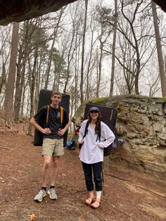 a man and woman standing next to each other in the woods