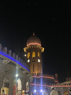 people standing in front of a building with a clock on it's tower at night