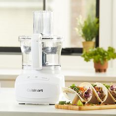 a food processor sitting on top of a counter next to some vegetables and burritos