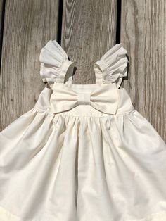 "Beautiful Big Bow Girls dress. Made of 100% cotton, Back has elastic for comfort and a great fit. This dress is a must have for your child's wardrobe. Also makes a beautiful gift! The listing is for one bow dress! These are the APPROXIMATE measurements of my dresses from shoulder to hem: size/chest/length 0-3m / 14\"/13\" 3-6m /16/14\" 6-9m /17\"/15\" 9-12m /18\"/16\" 12m-18m /19\"/17.5\" 18m-24m /20\"/19\" 2t /21\"/20\" 3t /22\"/20.5\" 4t / 23\"/22\" 5t /24\"/23\" 6y / 25\"/24\" 7y / 26\"/25\" White Cotton Dress With Tie Back, Beige Summer Dresses With Bow, White Bow Dress For First Birthday, White Dress With Bow For First Birthday, Spring Dress With Bow And Flutter Sleeves, Cotton Dress With Bow Tie Back For Garden Party, White Satin Bow Dress For Spring, White Dresses With Satin Bow For Spring, White Spring Dresses With Satin Bow