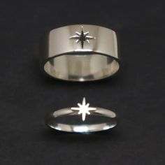 two silver rings sitting next to each other on top of a black surface and one has a star in the middle