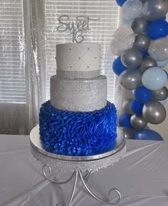 a three tiered cake with blue and silver frosting on top, surrounded by balloons