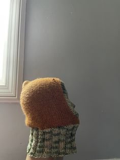 a stuffed animal wearing a knitted hat in front of a window with sunlight coming through it