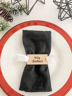 a christmas place setting with black napkins and silverware on a red rimmed plate