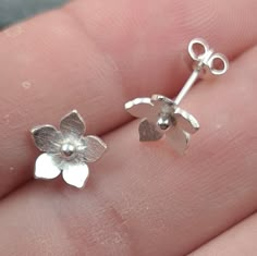 Little tiny silver flowers, they could be cherry blossom or forget-me-nots, on simple ear wires. Each one of these blossoms is handcut from textured sterling silver sheet before being shaped and securely soldered to an ear wire. There are several finishing and polishing stages before I carefully match a pair for you. Choose from perfectly polished or interestingly oxidised, each one will be unique. The little flowers measure approximately 9mm across and have a post 11mm long with a butterfly/scr Simple Silver Earrings Studs, Silver Wire Jewelry, Simple Silver Earrings, Art Clay Silver, Metal Jewelry Making, Shopping Wishlist, Silver Pooja Items, Silver Flower Earrings, Metal Clay Jewelry