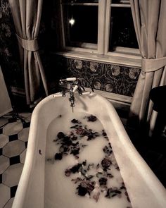 the bathtub is filled with rose petals in front of two windows and curtains that have drapes on them