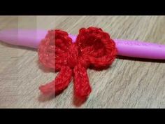 a crocheted red bow sitting on top of a wooden table next to a pink pen