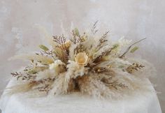 an arrangement of dried flowers and feathers on a white tablecloth with a gray wall in the background