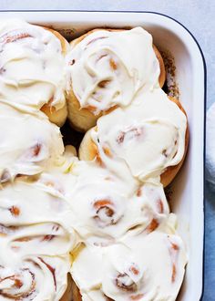 a white dish filled with cinnamon rolls covered in icing