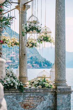 an outdoor wedding setup with flowers and birdcages hanging from the ceiling, overlooking the water