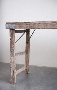 an old wooden bench sitting on top of a cement floor next to a white wall