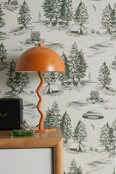 an orange lamp sitting on top of a wooden table next to a wallpaper covered in trees