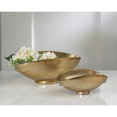 two gold bowls with flowers in them on a marble countertop next to a white wall