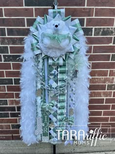 a teddy bear made out of paper and feathers hanging on a brick wall in front of a building