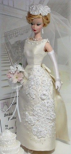 a barbie doll in a wedding dress and veil next to a cake with flowers on it