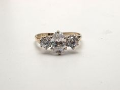 This impressive ring is set with simulated diamonds. I've listed them as cubic zirconia but they could be spinal. The centre stone is an oval that measures 8.5 X 5.8mm and the flanking stones are 4mm brilliant cuts. The total weight of the stone (if they were diamonds) would be 2ct. The shank is hallmarked 9ct gold with white gold settings. it weighs 2 grams and is a size Q now (US size 8) but I can size it up or down without further cost. It's refinished as new and so would be suitable as a gif Classic Oval Crystal Ring With Center Stone, Classic Oval Three Stone Cluster Ring, Elegant Three Stone Crystal Ring For Formal Occasions, Classic Cubic Zirconia Topaz Ring For Anniversary, Classic Oval Cubic Zirconia Ring, Classic Oval Topaz Ring For Anniversary, Oval Diamond Cut Topaz Ring For Anniversary, Oval Diamond Cut Topaz Anniversary Ring, Classic Oval Topaz Ring With Center Stone