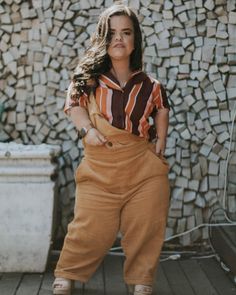 a woman standing on a wooden floor next to a pile of rocks wearing brown overalls