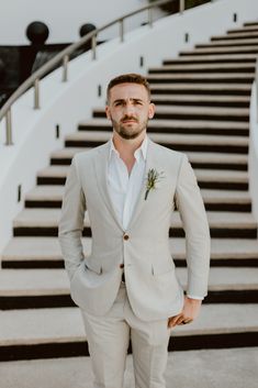 a man standing in front of some stairs wearing a white suit and flower boutonniere