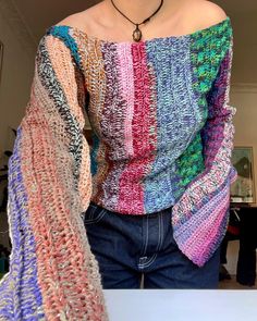 a woman wearing a multicolored sweater standing next to a white table with a necklace on it