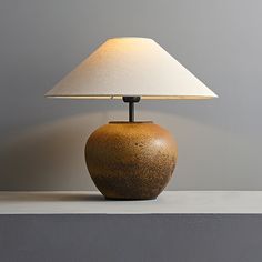 a lamp sitting on top of a table next to a gray wall with a white shade