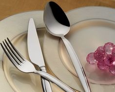 a white plate topped with silverware next to a pink flower on top of a table