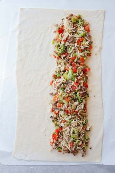 a long piece of food on top of a white paper covered in shredded cheese and veggies