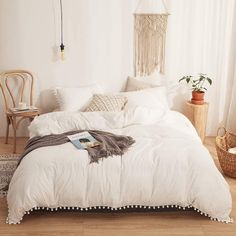 a bed with white comforter and pillows in a room next to a chair, potted plant and wicker basket