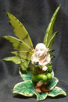 a fairy figurine sitting on top of a green leafy plant with leaves