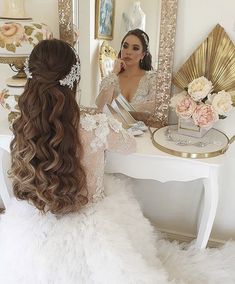 a woman sitting at a table in front of a mirror with her hair styled up