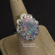 This remarkable Platinum Vintage Ring features a rare large black opal as its center piece. This specimen has a very even medium sized splashes of bright reds blues and greens play-of-color! The black opal is surrounded by a fancy floral like diamond pattern designs. Ring Size: 6.25 Total Weight: 15.75 grams Face Size: 1.1 inch x 0.9 inch Precious Metal: Platinum Precious stones: -Black Opal Center Stone: 6.17 carats, 18.1mm x 13.1mm -White Round Diamonds 0.78 carats Hallmark: Pt900 6.17 D0.78 Heirloom Multicolor Oval Jewelry, Oval Opal Jewelry Collectible, Elegant Multicolor Opal Ring, Collectible Oval Opal Jewelry, Formal Multicolor Opal Gemstone Ring, Formal Multicolor Opal Ring, Elegant Multicolor Cabochon Opal Ring, Elegant Oval Untreated Opal Ring, Multicolor Oval Opal Ring For Formal Occasions