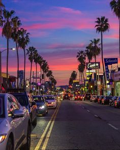 cars are parked on the street in front of palm trees and shops at sunset or dawn