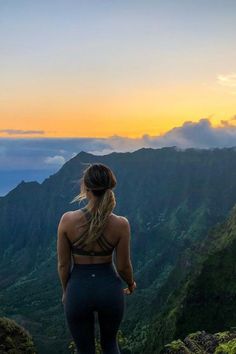 a woman standing on top of a mountain looking at the sky and mountains in the distance