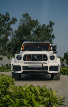 the front end of a white truck parked on top of a cement road next to bushes