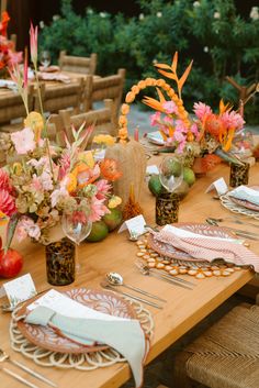 the table is set with place settings and flowers in vases, plates, napkins