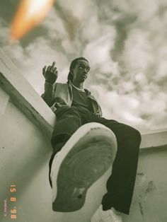 a black and white photo of a man sitting on the edge of a building with his feet up