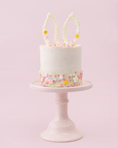 a white cake with pink and yellow flowers on the top is sitting on a pedestal