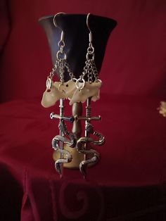 Coyote atlas vertebrae earrings with dangling sword. Available in gold or silver chains Available in shepherd's hooks or leverback hooks Due to the bones being real, they will slightly vary in size and color on each pair Bones are scrubbed with soap and water and cleaned with peroxide.  We do not use bleach or anything else that will weaken them Bone Colored Metal Earrings For Pierced Ears, Unique Bone-colored Nickel-free Earrings, Nickel-free Bone Dangle Earrings, Nickel-free Bone-colored Dangle Earrings, Symbolic Dangle Plug Earrings For Pierced Ears, Nickel Free Bone Color Dangle Earrings, Handmade White Gothic Earrings, White Gothic Handmade Earrings, Atlas Vertebrae