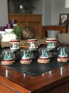 there are four glass jars on top of a table with christmas trees in the middle