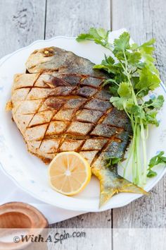 grilled fish on a white plate with garnishes and lemon wedges