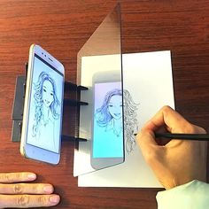 a person drawing on paper with a cell phone next to it and another hand holding a pen