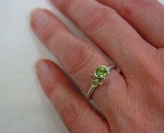 A beautiful bright green 5 mm peridot is set into a split bezel on one of my textured stacking rings. Next to the stone sits a single hydrangea blossom cast in solid 18k gold. The perfect little hydrangea measures just 6mm and it sits on a 1.9mm wide sterling band that is detailed with some tool marks and textures that give it a slightly primitive feel. The ring has a soft, satin, burnished finish. This ring can be stacked with most of my other rings, the last photo shows it stacked with my hydr Hallmarked Peridot Ring Jewelry, Lime Green Peridot Ring For May Birthstone, Unique Multi-stone Peridot Rings, Lime Green Peridot Rings Fine Jewelry, Luxury Peridot Three-stone Rings, August Birthstone, Botanical Jewelry, Peridot Ring, Gold Floral