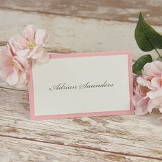 some pink flowers and a white card on a wooden table