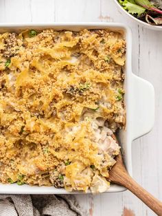 a casserole dish with meat and vegetables in it next to a bowl of salad