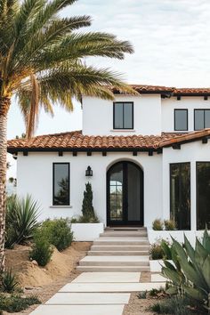 a white stucco house with palm trees in the front yard and steps leading up to it