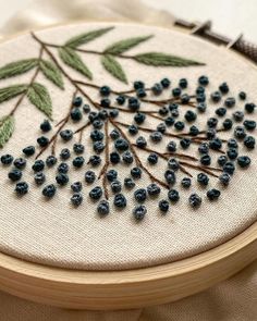 a close up of a embroidery on a wooden hoop with blue beads and green leaves