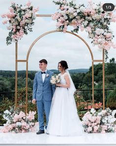 a bride and groom standing in front of an arch decorated with pink flowers on their wedding day